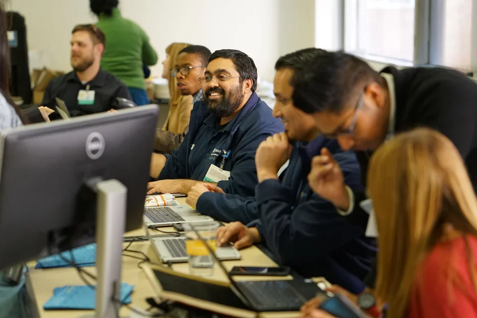 A diverse group of individuals diligently working on computers in a well-lit classroom setting.